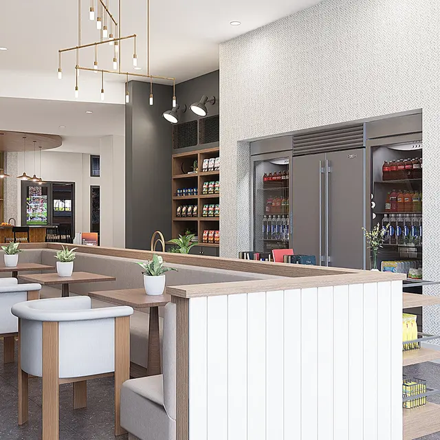 A modern cafe interior featuring a light color palette, with a bar counter, white stools, and shelves holding various products. The space is well-lit and has an open layout with a kitchen area visible in the background.