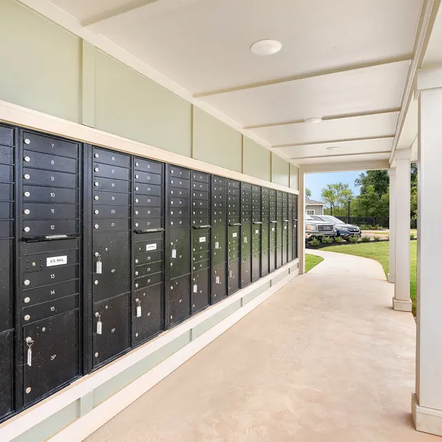 A row of black mailboxes mounted on a wall in a covered outdoor area, with a landscaped lawn visible in the background.