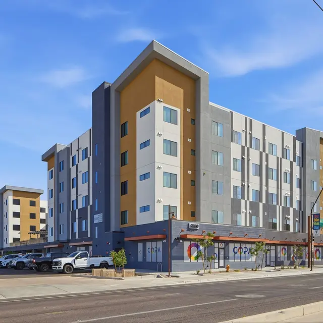 Modern Apartment Complex A contemporary four-story apartment complex with a modern design, featuring a mix of beige and gray panels under a blue sky.