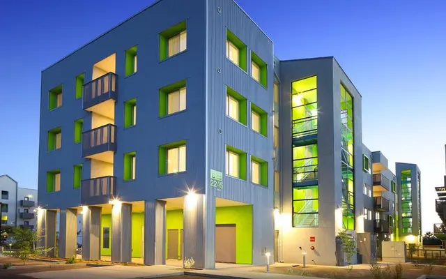 Vibrant Modern Apartment Building A modern apartment building with unique design featuring a combination of blue and green colors. The building has multiple levels with balconies and large windows. Soft lighting enhances the architectural details in the evening.