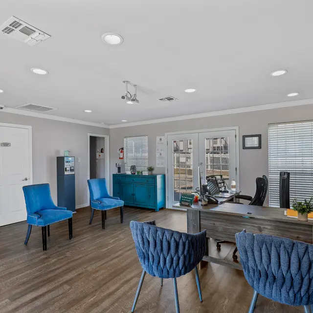 A modern office reception area with blue chairs, a wooden desk, and natural light from large windows.