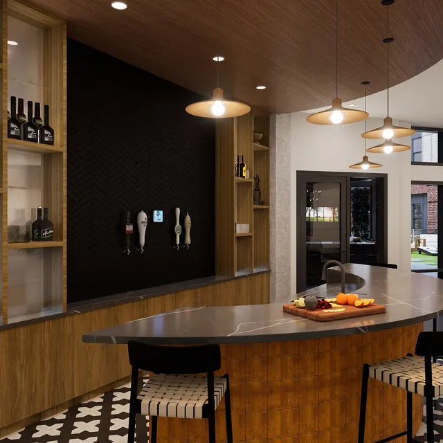 A modern kitchen bar area featuring a curved countertop, wooden shelves with wine bottles, and stylish lighting. There are bar stools with a unique pattern, and large windows in the background revealing an outdoor space.