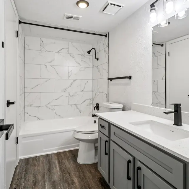 A modern bathroom featuring a bathtub with marble tiles, a sleek gray vanity with a white countertop, and contemporary fixtures.
