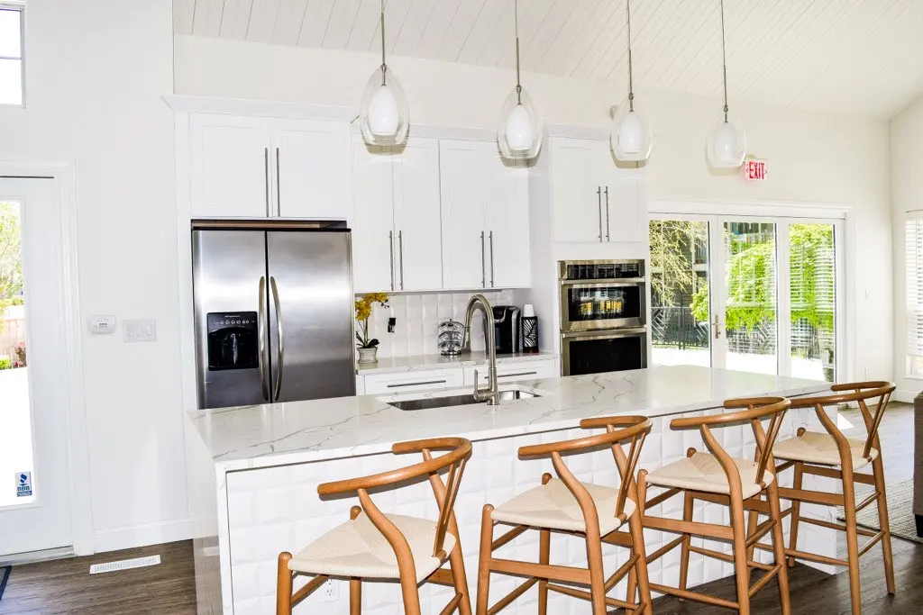Modern Kitchen Interior A modern kitchen with a large island, white cabinetry, stainless steel appliances, and wooden bar stools. Natural light floods the space through large windows