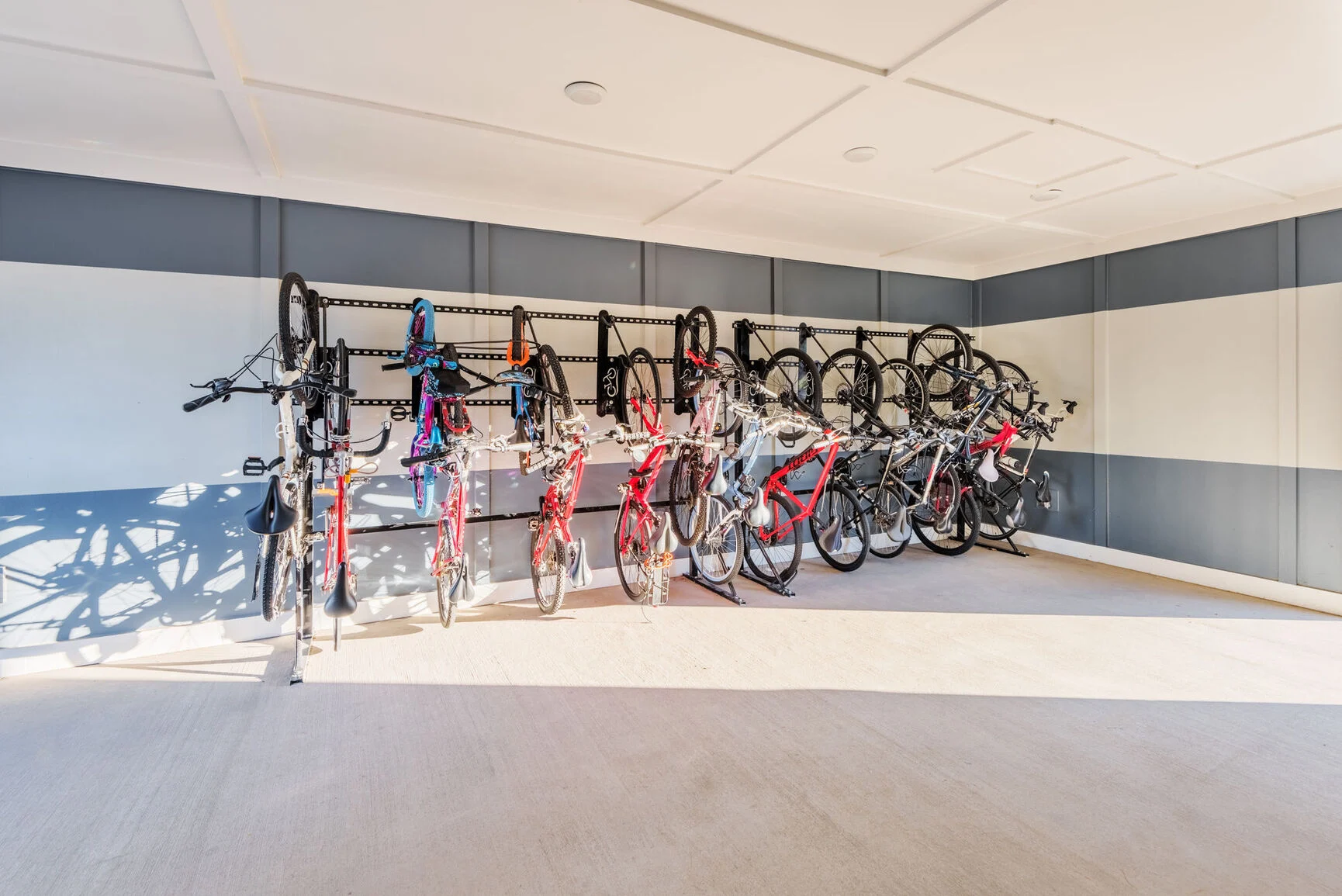 Bicycle Storage Area A well-organized bicycle storage area featuring several bikes hanging on racks against the wall. The space is brightly lit and has a modern design with a striped wall.