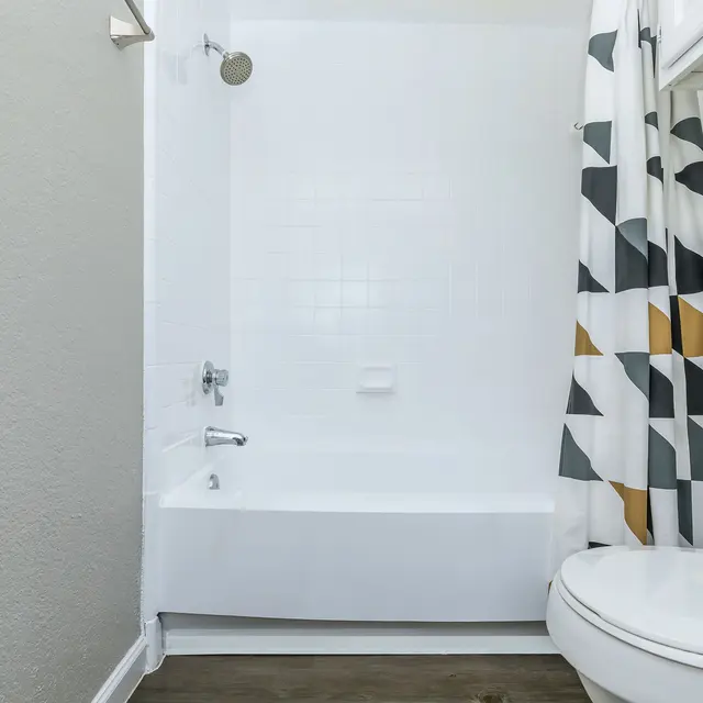 A modern bathroom featuring a white tub and shower combination with a geometric patterned shower curtain. The bathroom has light colored walls and a sleek toilet.