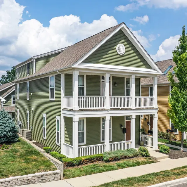 Green Two-Story House Exterior A two-story green house with white trim, featuring a front porch and multiple windows. It is surrounded by grass and landscaping.