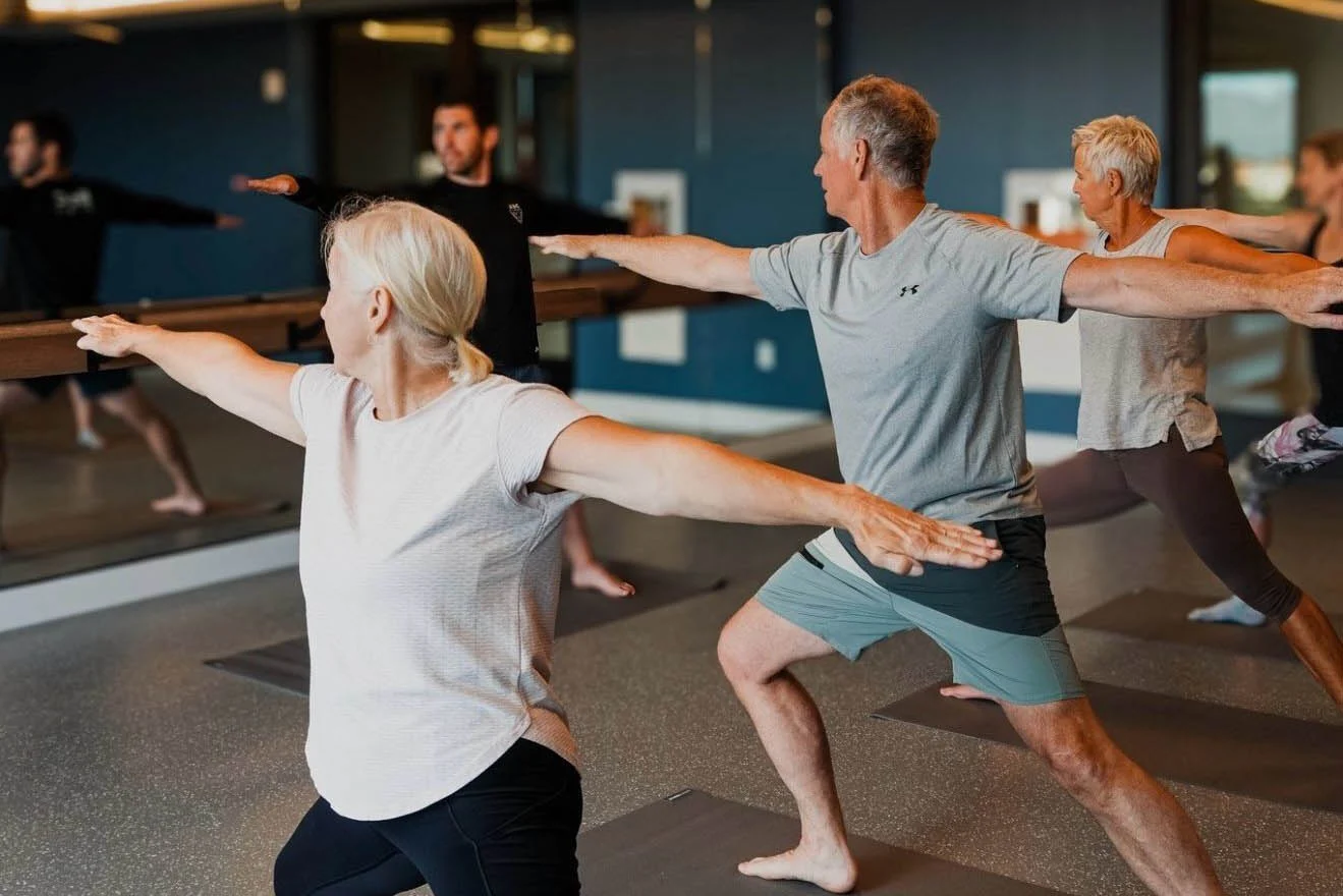Yoga Class in Session A group of individuals participating in a yoga class, performing poses in a studio with mirrors and modern decor.