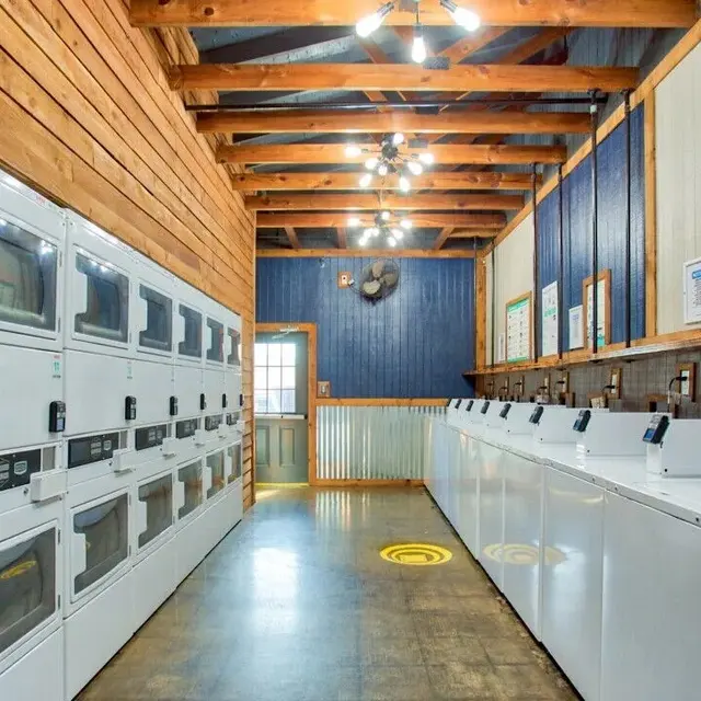 Interior view of a laundry room with stacked washing machines and dryers against wooden walls and ceiling.