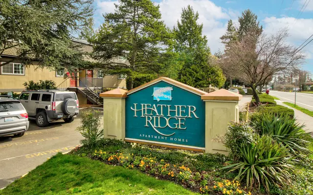 Heather Ridge Apartment Homes Sign for Heather Ridge Apartment Homes with surrounding greenery and parked vehicles
