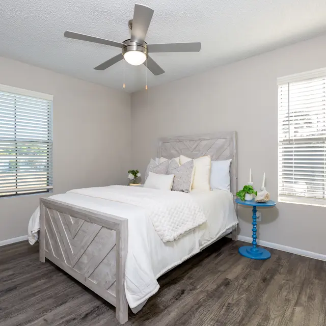 Cozy bedroom with a bed, blue side table, and large windows.
