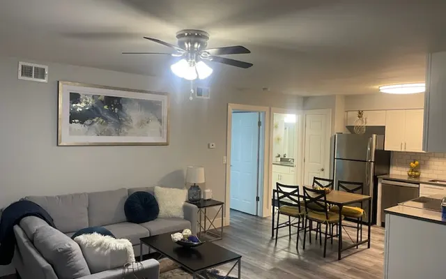 A stylish and modern living area featuring a gray sofa, coffee table, and a dining area with black chairs and a kitchen in the background.