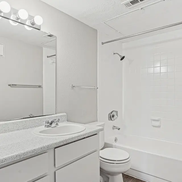 A clean and modern bathroom featuring a white tub, sink, and vanity with a mirror and lighting above.
