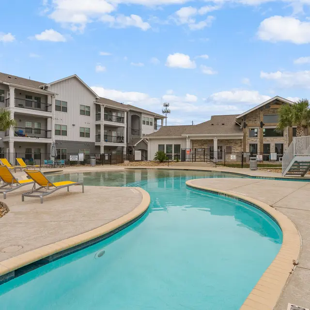 View of a modern apartment complex pool with a curved lagoon-style pool and lounge chairs.