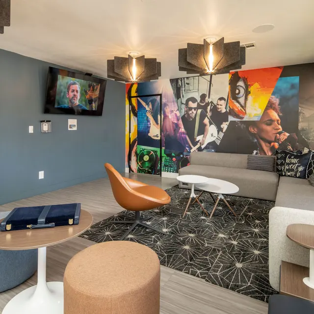 Modern lounge area with a gray couch, colorful wall art, stylish lighting, a flat-screen TV, and contemporary furniture.