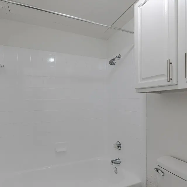 A bright and clean bathroom featuring a white bathtub and shower, white tiled walls, and a modern cabinet above the toilet.