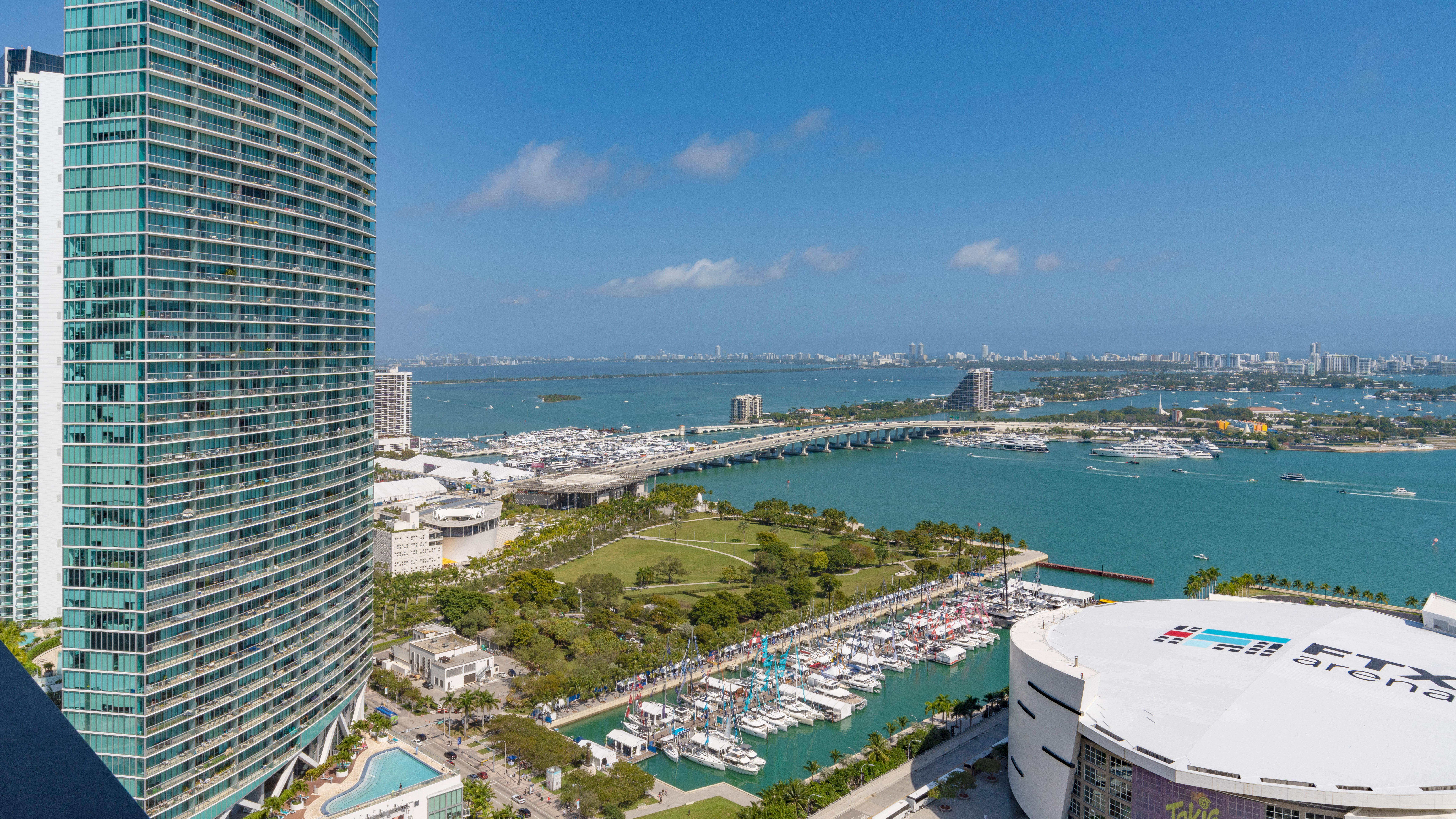 Panoramic View of Miami Waterfront A panoramic view of a waterfront city featuring tall buildings, a marina with boats, and a vibrant blue ocean under a clear sky.