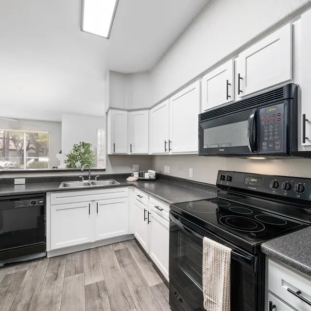 Modern kitchen with white cabinetry, black appliances, and spacious countertops at Bear Canyon Apartments in Tucson