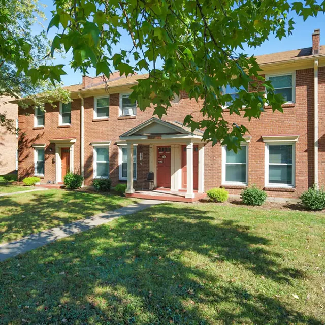 Row of brick apartment buildings with green lawn and trees.