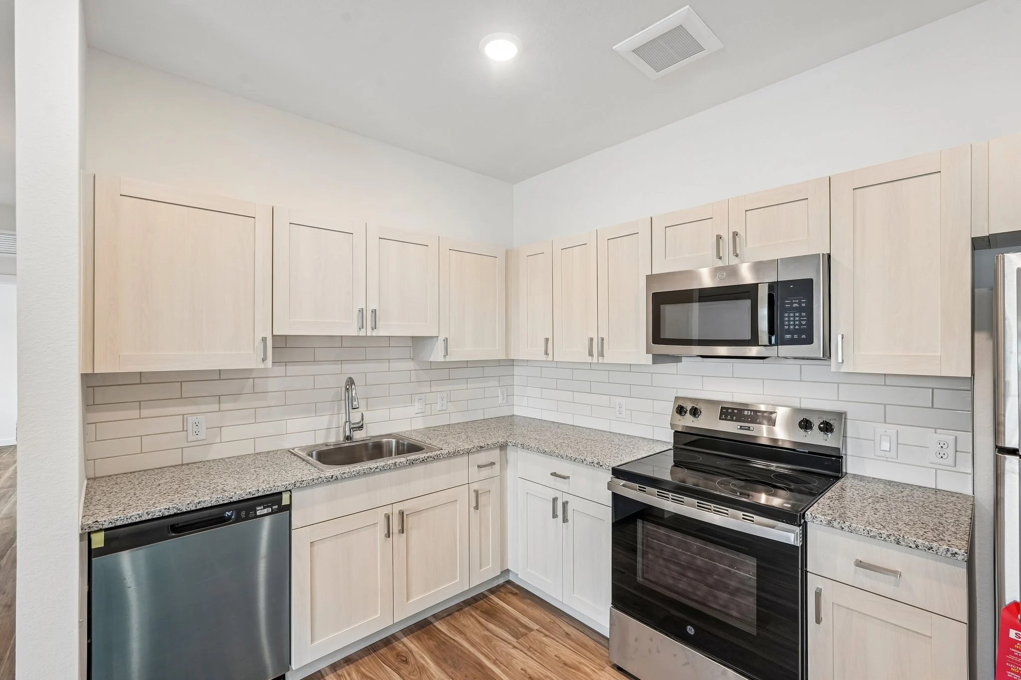 A modern kitchen featuring light wood cabinets, granite countertops, and stainless steel appliances including a dishwasher and oven.