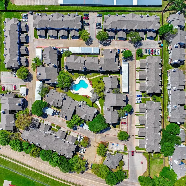 Aerial view of a residential apartment complex featuring multiple buildings, a swimming pool, and green areas. Adjacent to a water body.