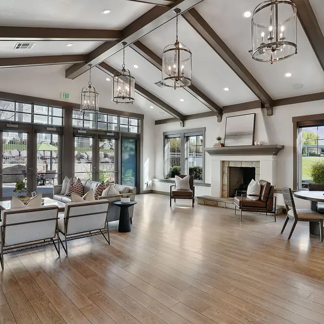 A spacious modern living room featuring high ceilings with wooden beams, large windows allowing natural light, a cozy fireplace, and stylish furniture arranged for comfortable seating.