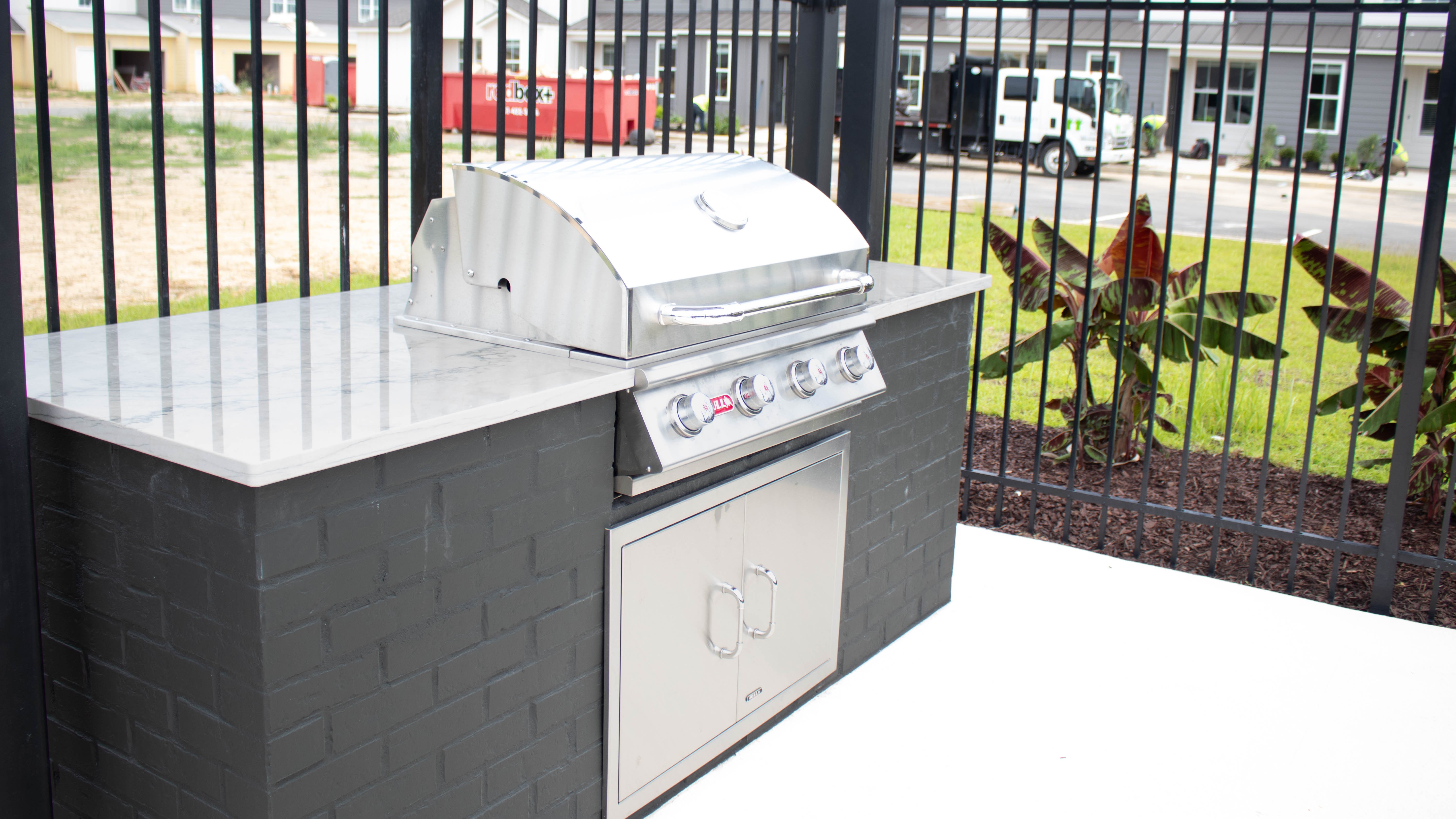 An outdoor grilling station featuring a stainless steel grill and a stone countertop with a storage cabinet underneath.
