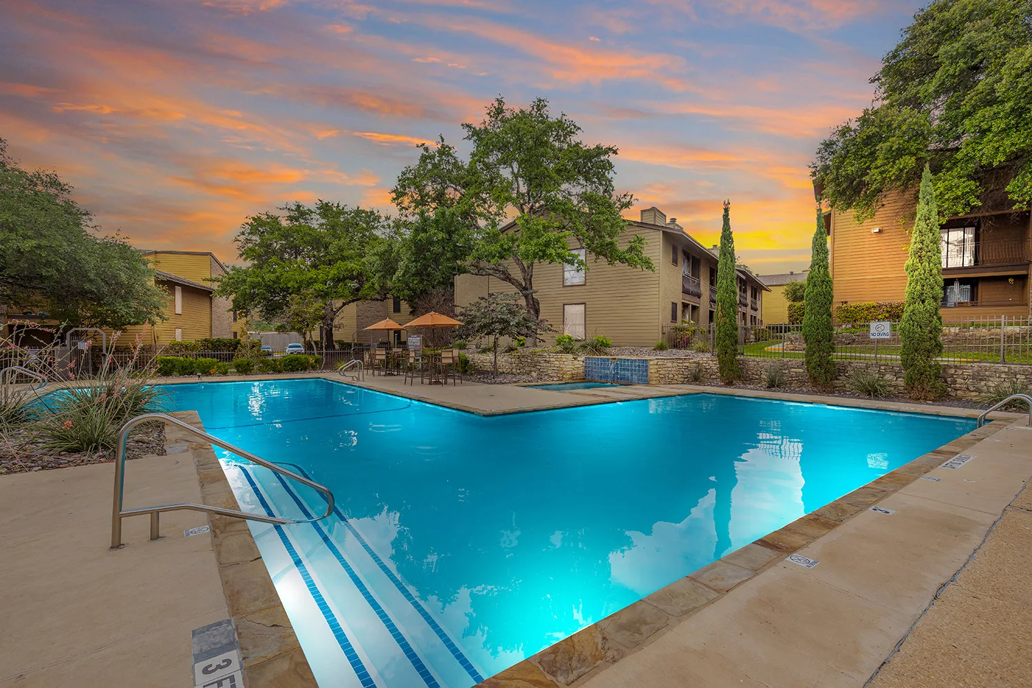 A serene pool area surrounded by greenery and buildings during sunset.