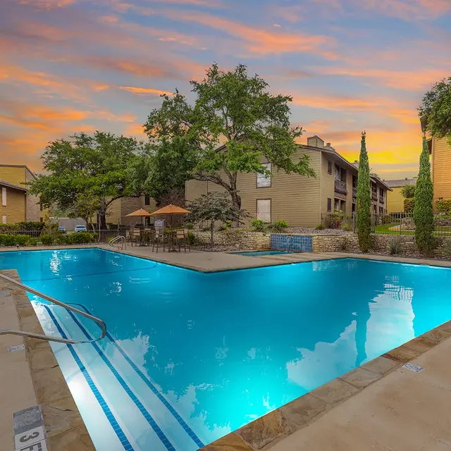 A serene pool area surrounded by greenery and buildings during sunset.