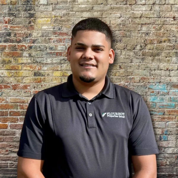 Portrait of a Smiling Man A smiling man standing in front of a textured brick wall, wearing a black polo shirt with a logo.