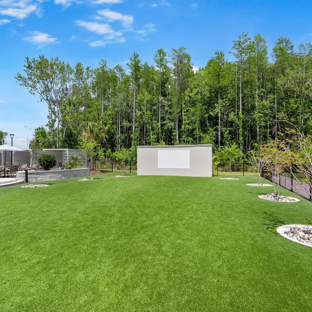Park Landscape with Green Grass and Trees A grassy area in a park featuring a light-colored wall, surrounded by trees and a fence.