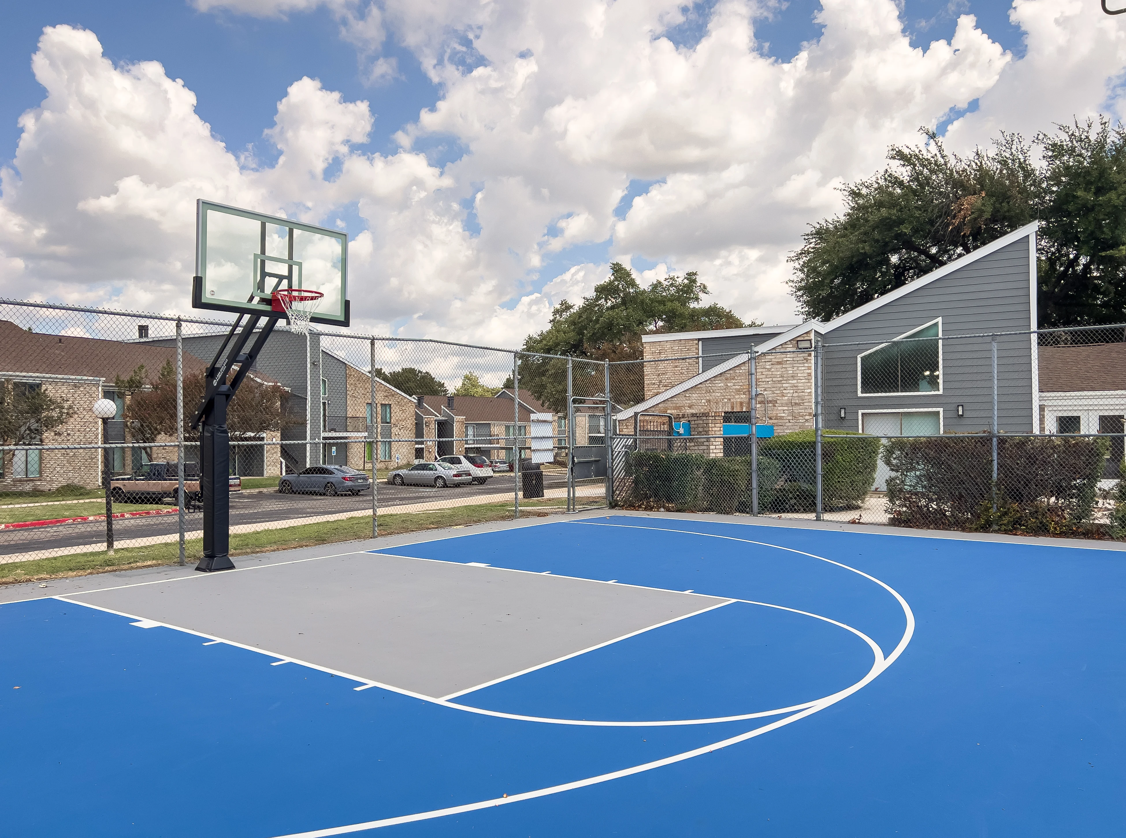 Outdoor Basketball Court A bright blue outdoor basketball court with a hoop, surrounded by a fence and buildings in the background.