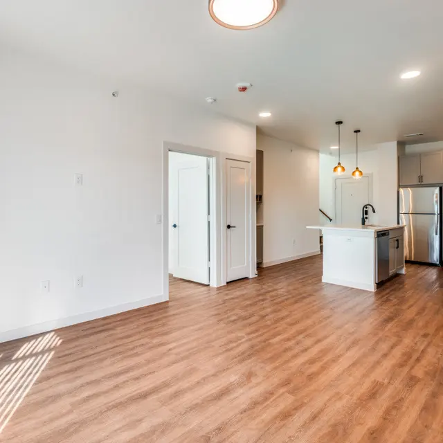 A spacious and modern apartment interior featuring a light color scheme, wooden flooring, an island kitchen, and bright natural light.