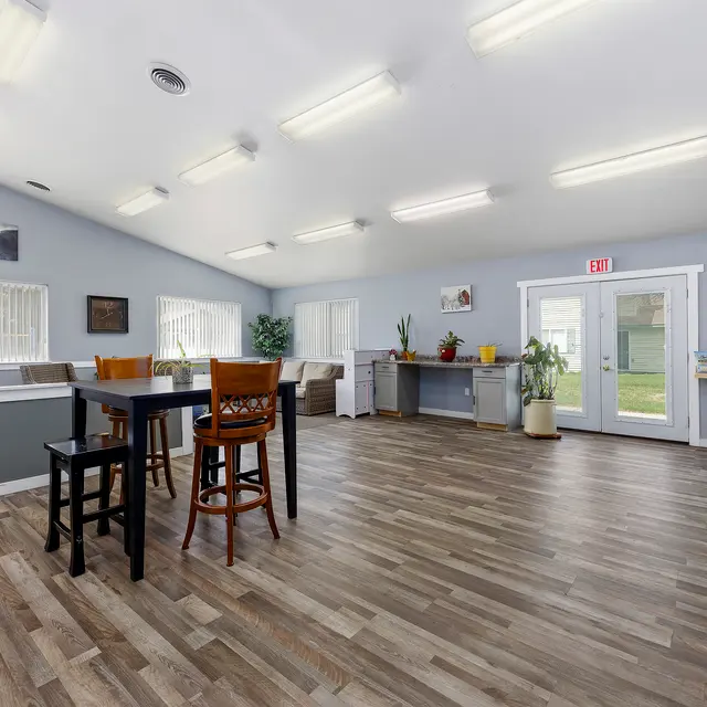 Interior of a Community Room Interior view of a community room with wooden flooring, tables and chairs arranged, and large windows allowing natural light.