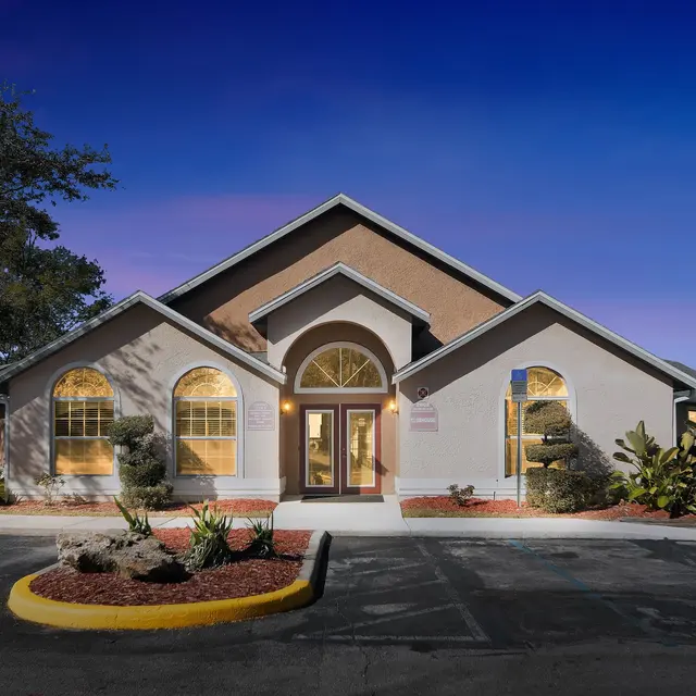 Exterior view of a modern building at night with illuminated windows and landscaped surroundings.