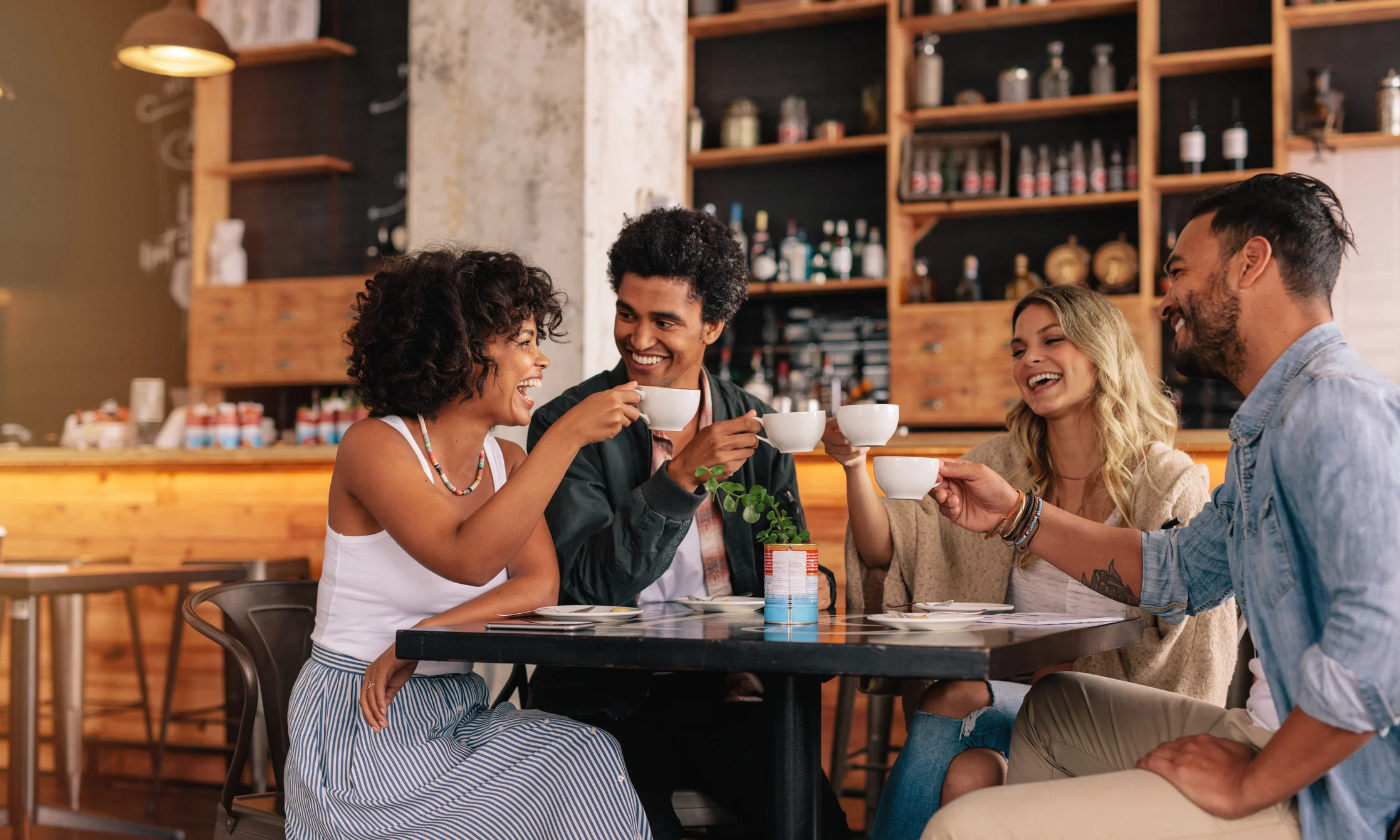 Joyful Café Gathering Four friends gathered around a table in a cozy café, smiling and holding coffee cups.