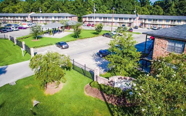 Aerial view of a motel with two-story buildings and a parking area in front, surrounded by green grass and trees.