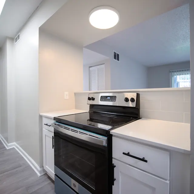 A modern kitchen featuring a black stove with a sleek design, white cabinetry, and light gray walls. The space is well-lit with natural light and has a minimalist aesthetic.