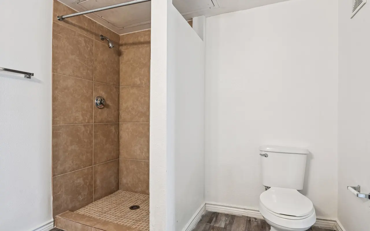 A modern bathroom featuring a shower area with beige tiles and a white toilet. The shower is partially enclosed with a partition wall.