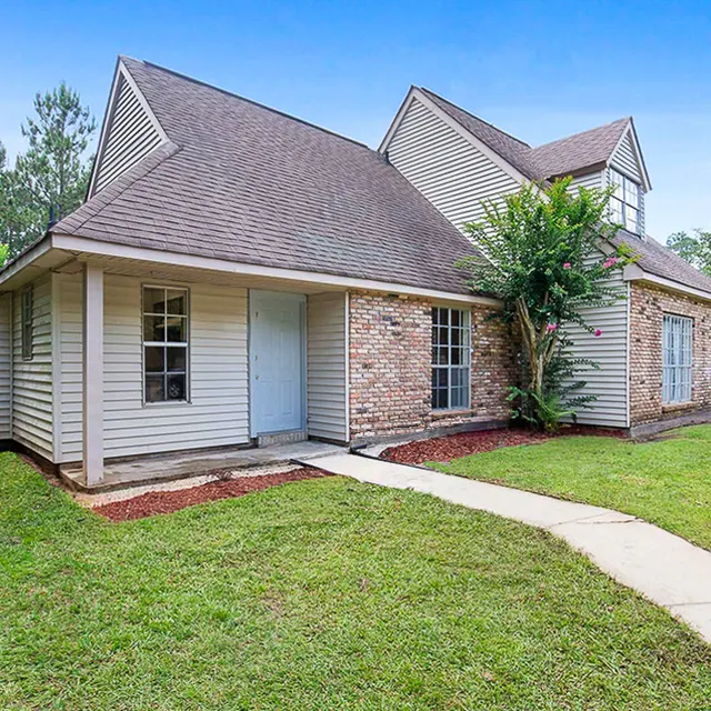 A single-family home with a combination of brick and siding exterior, surrounded by a grassy lawn and trees.