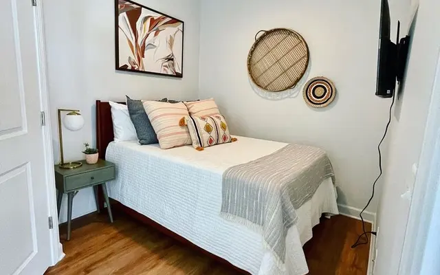 A cozy bedroom featuring a bed with decorative pillows, a wall-mounted TV, and artistic wall decor
