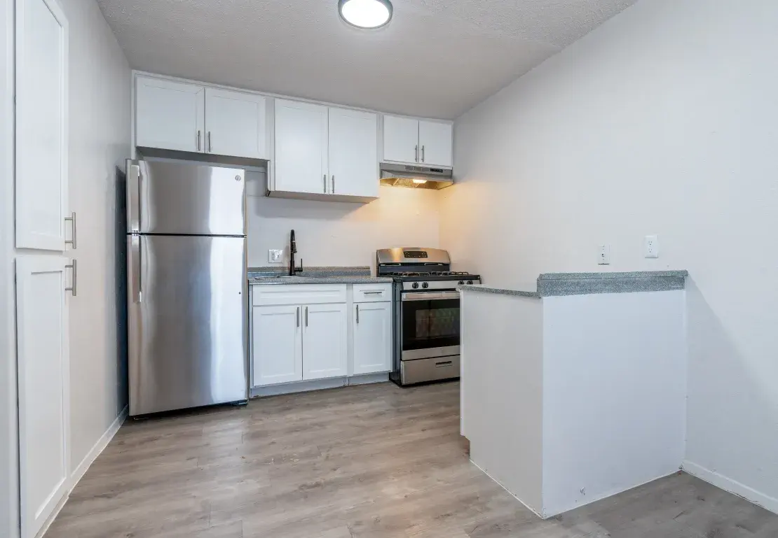 Modern Kitchen with Stainless Steel Appliances A modern kitchen with white cabinets, stainless steel appliances, and wooden flooring. The kitchen features a refrigerator, stove, and a small bar area.