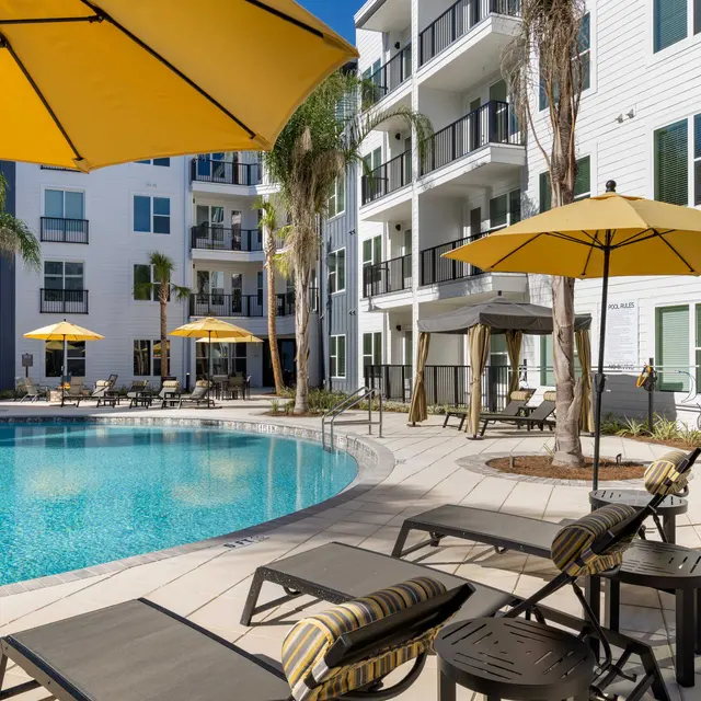 A sunny apartment complex pool area with lounge chairs and yellow umbrellas surrounding the pool.