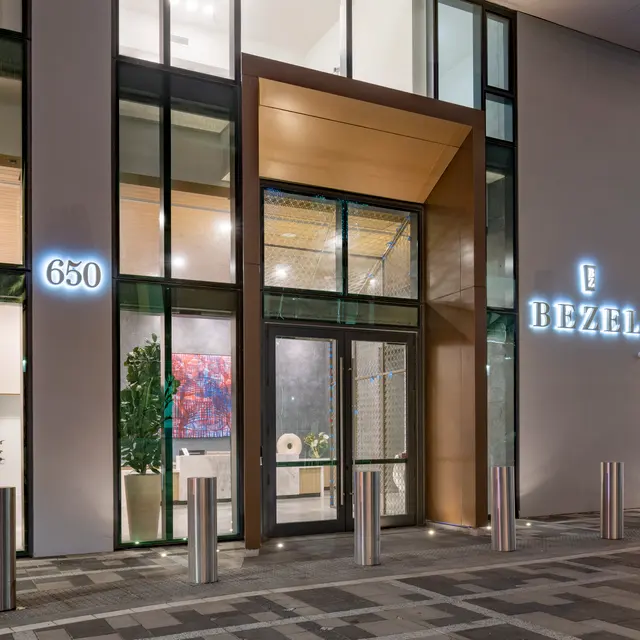 Modern building facade with large glass windows and a wooden entrance, featuring illuminated signage that reads 'Bezel' and the number '650'.