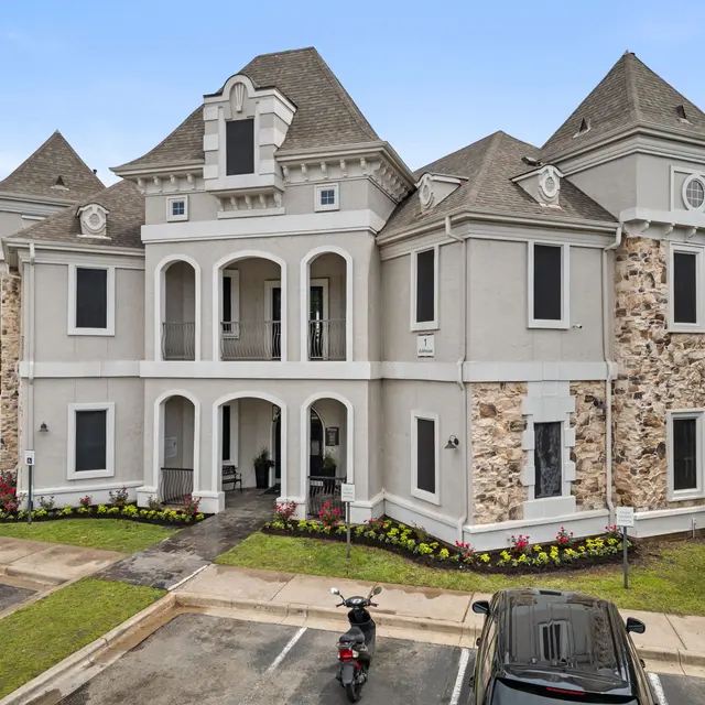 A grand Victorian-style building with stone accents and a landscaped front, featuring multiple gables and archways.