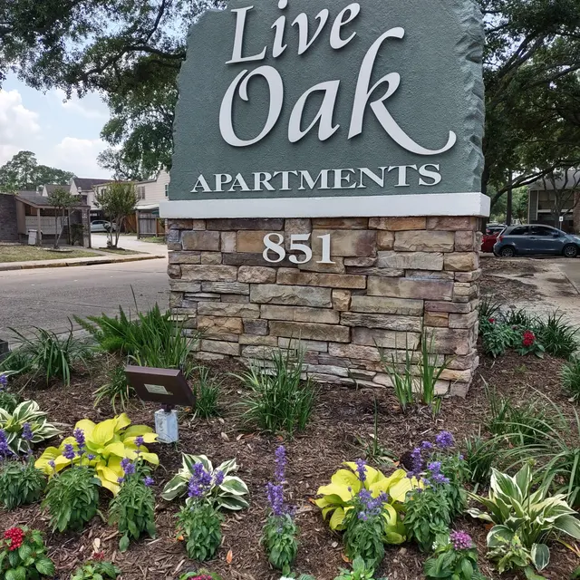Live Oak Apartments Entrance A stone sign for Live Oak Apartments featuring lush landscaping with colorful flowers in front.