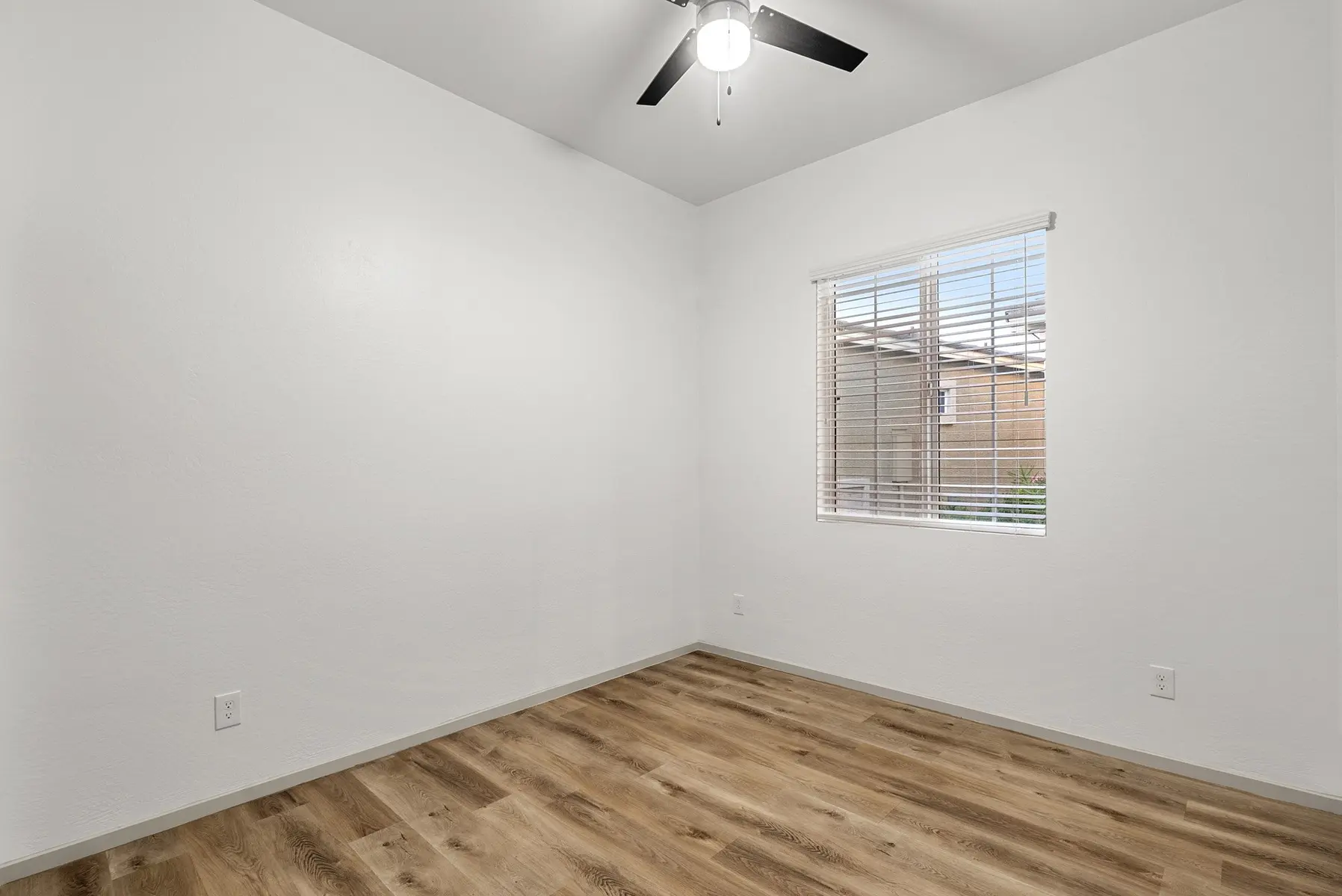 Empty room with white walls, a ceiling fan, a window with blinds, and light wooden flooring.