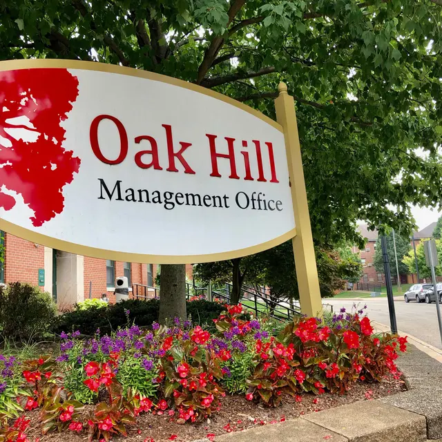 Oak Hill Management Office Sign A sign for Oak Hill Management Office featuring a red tree silhouette and vibrant flower beds in front.