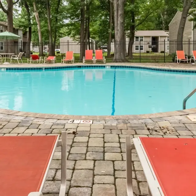 A swimming pool in an apartment complex surrounded by lounge chairs and trees.