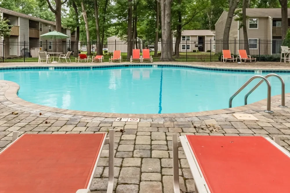 A swimming pool in an apartment complex surrounded by lounge chairs and trees.